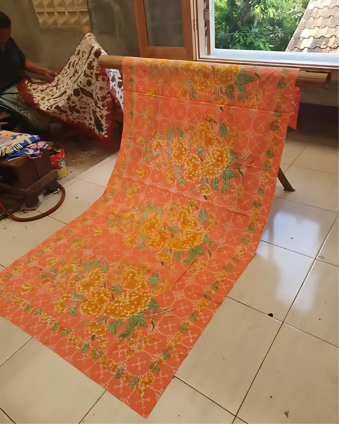 Sarung batik tulis katun primissima dengan motif bunga mekar berwarna kuning keemasan di atas dasar kain jingga yang hangat.