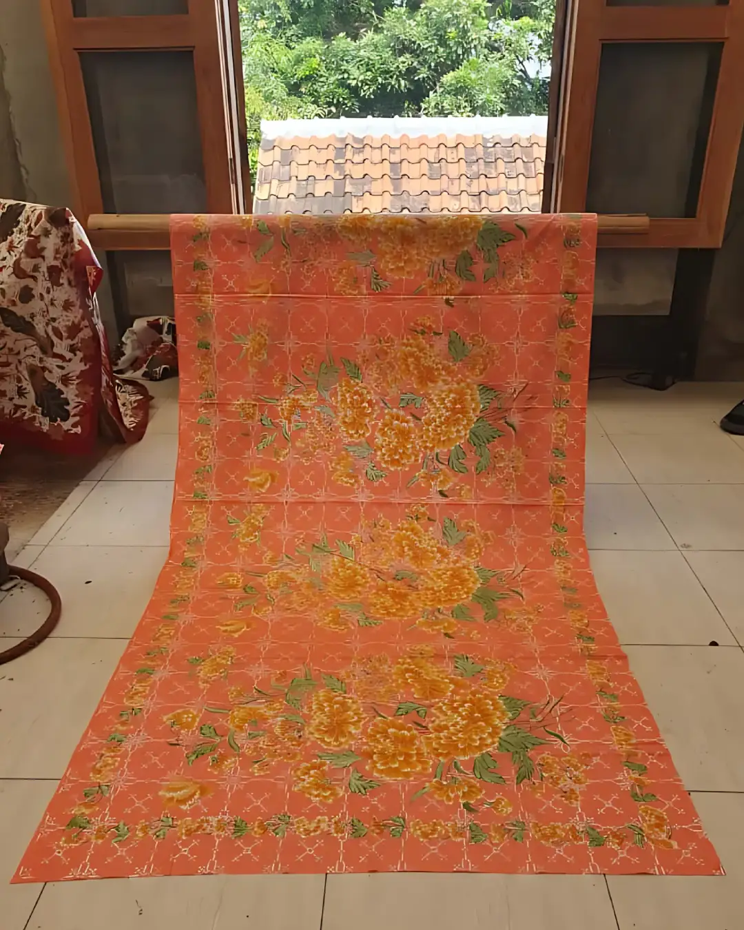 Sarung batik tulis katun primissima dengan motif bunga mekar berwarna kuning keemasan di atas dasar kain jingga yang hangat.